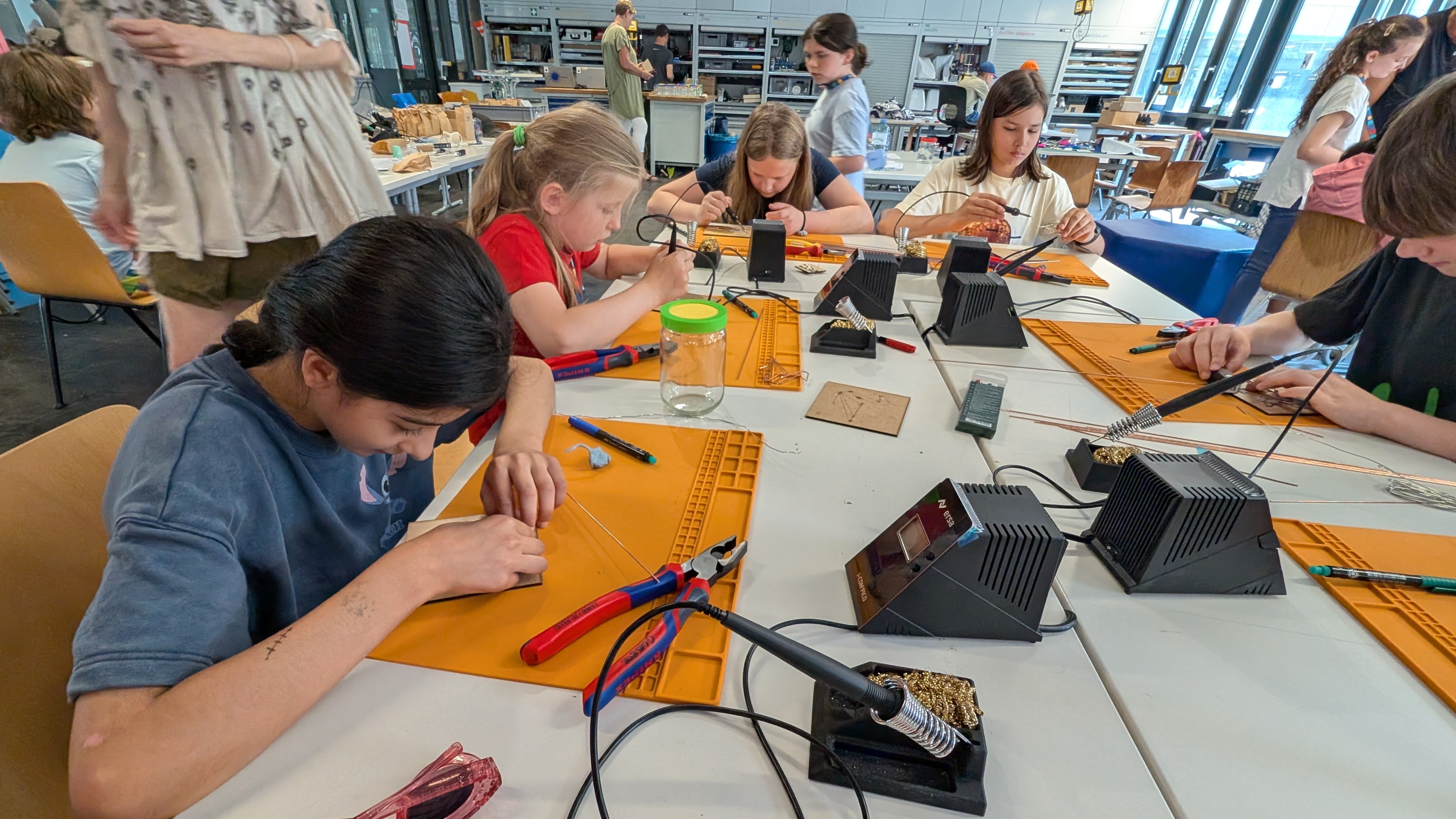 Schüler*innen sitzen im Labor um einem großen Tisch und löten