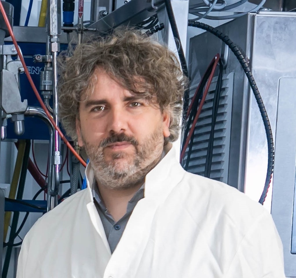 Porträt eines Mannes in Labor-Kittel vor einem großen Laborgerät