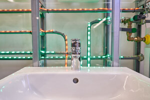 Waschbecken mit Mischbatterie und Rohren, die rot bzw. grün leuchten für Warm- oder Kaltwasser