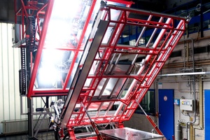 Der Solarkollektorenprüfstand in Aktion: Acht Lampen hinter einer großen Glasscheibe bilden die künstliche Sonne, die auf eine Trägerkonstruktion scheint. Die Gestänge des Geräts sind rot, die Lampen eingeschaltet.
