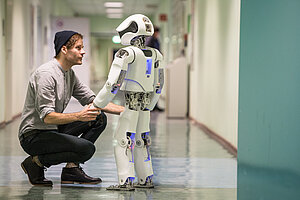Ein Mann und ein Roboter halten sich an den Händen uns sehen sich an