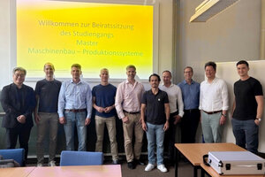 Zehn Männer posieren in einem Seminarraum