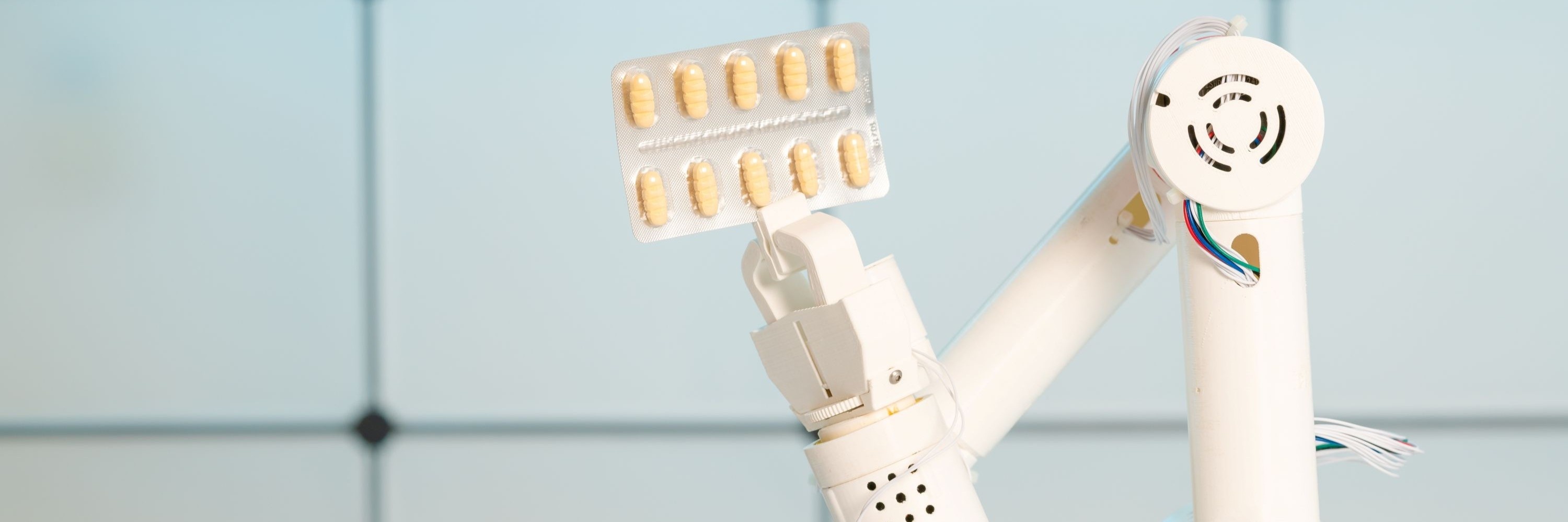Foto: Ein robotischer Greifarm hält eine Blisterpackung mit zweimal fünf Tabletten.