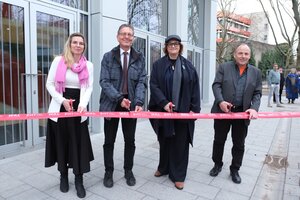Vier Personen stehen vor einem Gebäude und halten Scheren bereit, um ein rotes Band durchzuschneiden