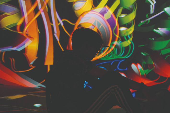 Schatten eines sitzenden Menschen mit VR-Brille vor bunter abstrakter Projektion, Text: Lange Nacht der Wissenschaften, 28. Juni 2025, 17-24 Uhr 