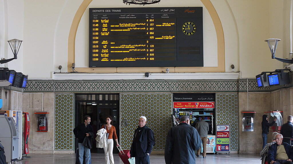 Menschen vor einer Bahnhofsanzeige in Marokko