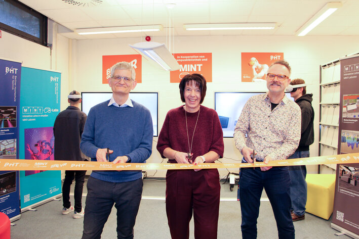 Drei Personen schneiden ein orangenes Band durch