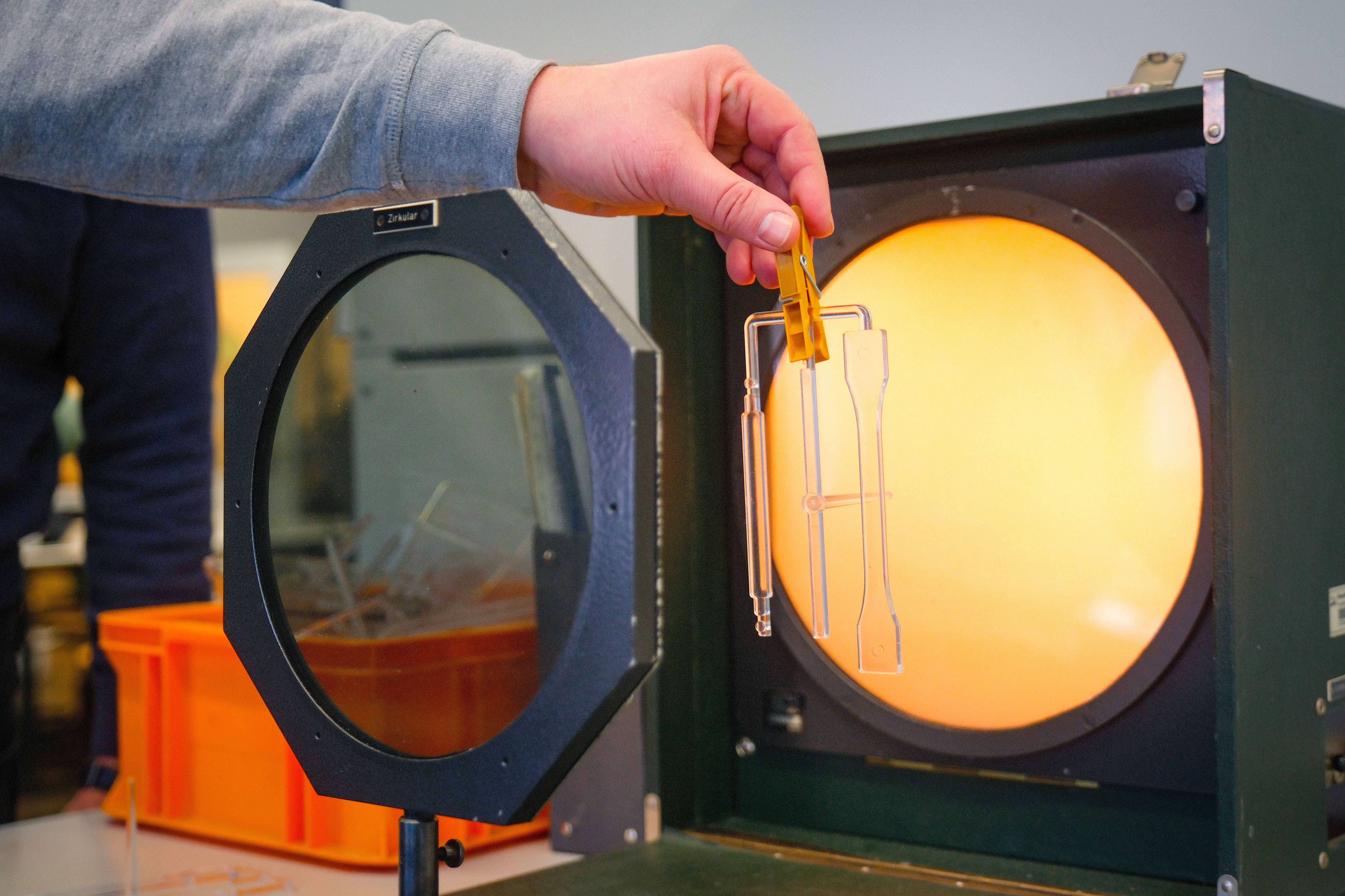 Jemand hält Kunststoffproben in die runde, erleuchtete Öffnung eines Prüfgeräts