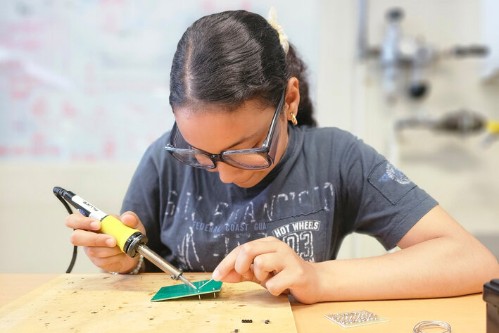 Ein Mädchen sitzt an einem Tisch und lötet. 