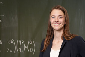 Frau steht vor einer Tafel mit mathematischen Gleichungen