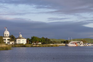 Blick über einen See ans andere Ufer, links Häuser mit USA Flagge auf dem Dach, rechts ein Schiff auf dem See.