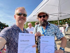 Zwei Männder mit Sonnenbrillen halten Urkunden in die Kamera