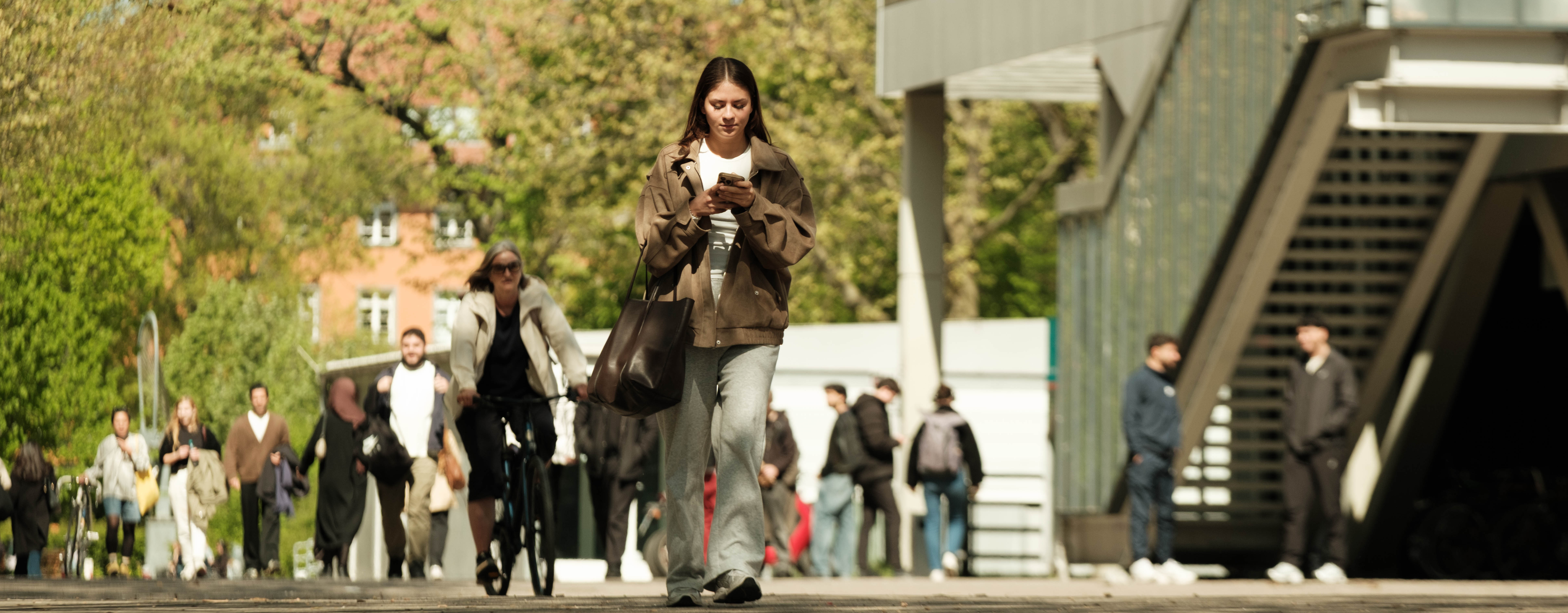 Eine Frau läuft über den belebten Campus der BHT, während sie auf ihr Handy schaut