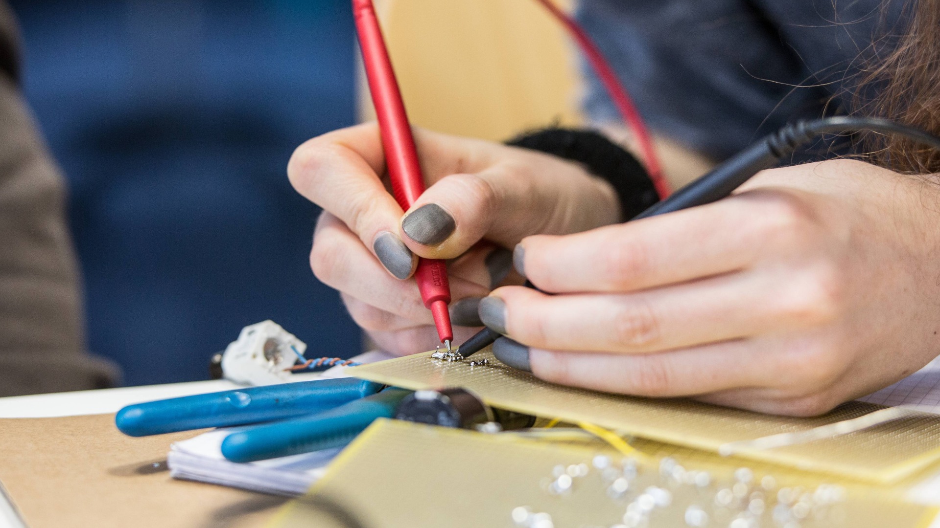 Hände mit lackierten Fingernägeln halten Lötkolben und löten etwas auf eine Platine