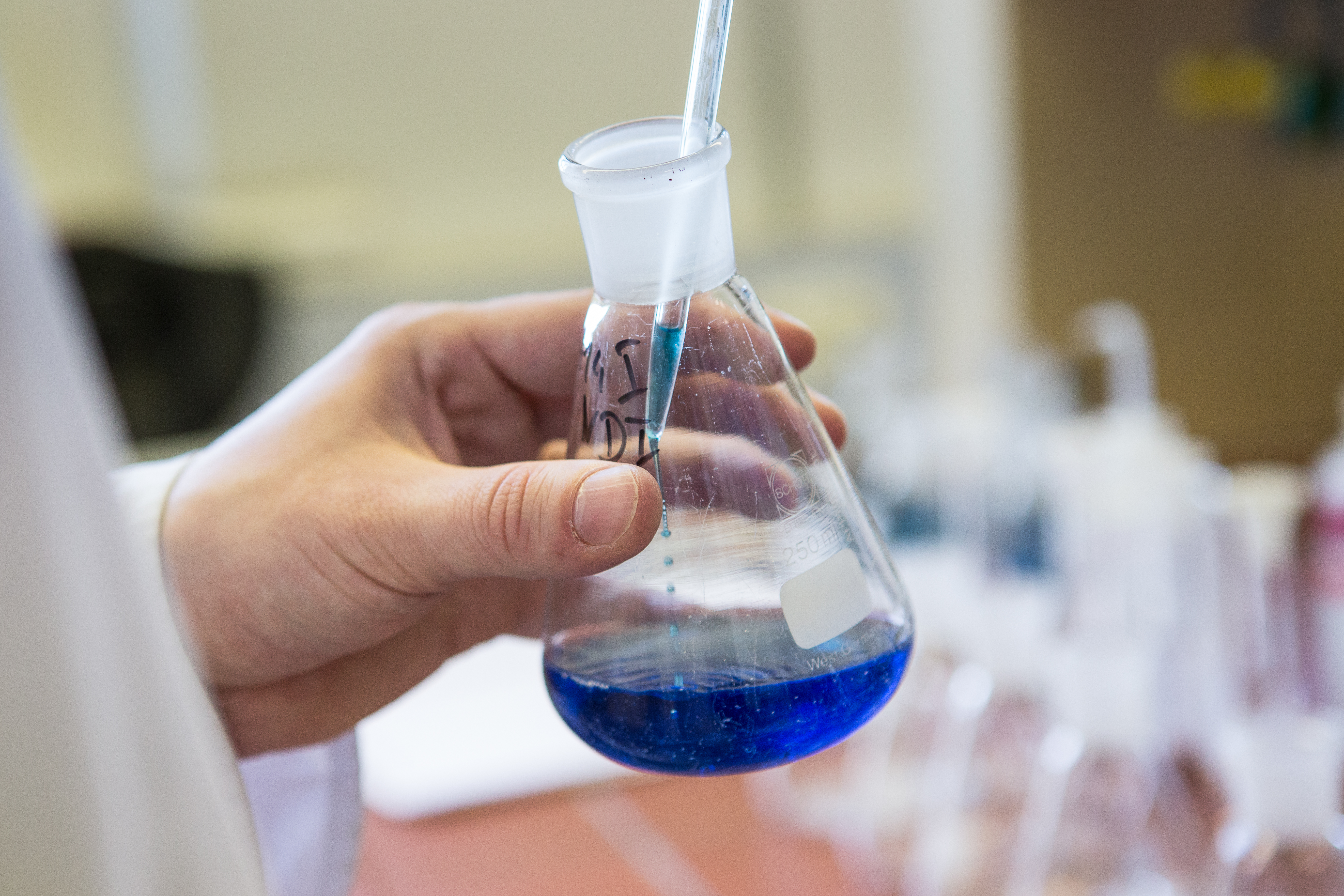 Person mit Kolben und blauer Flüssigkeit im Labor 