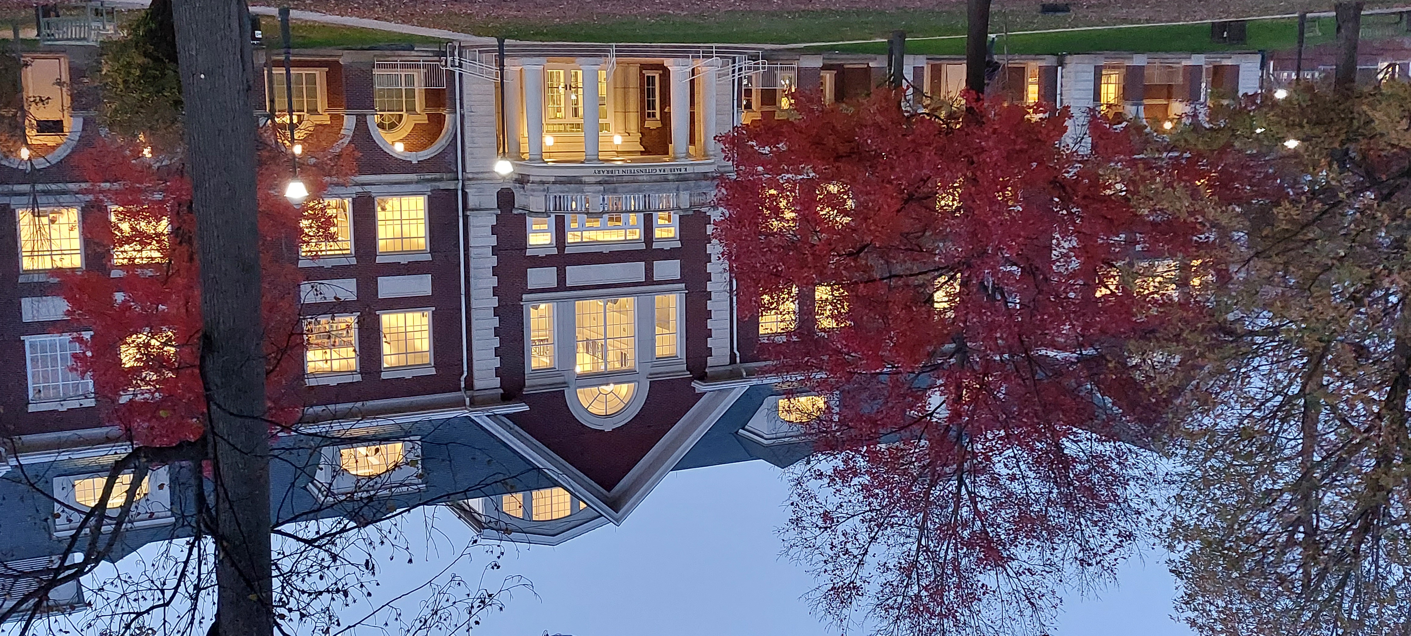 Säuleneingang eines klassischen Uni-Gebäudes in der Dämmerung, Licht strahlt durch Fenster, davon Rot-belaubte Bäume