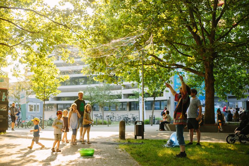 Kinder und Erwachsene sehen dabei zu, wie jemand riesige Seifenblasen macht auf dem grünen Campus der BHT