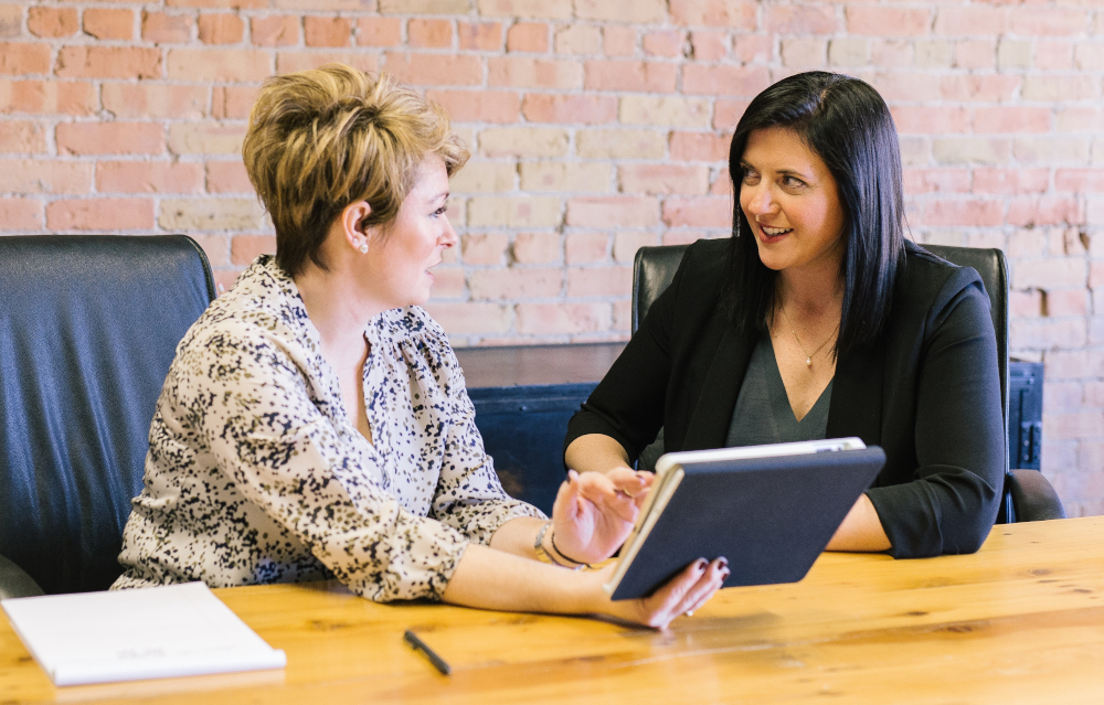 Zwei Frauen sitzen am Tisch und besprechen etwas. 