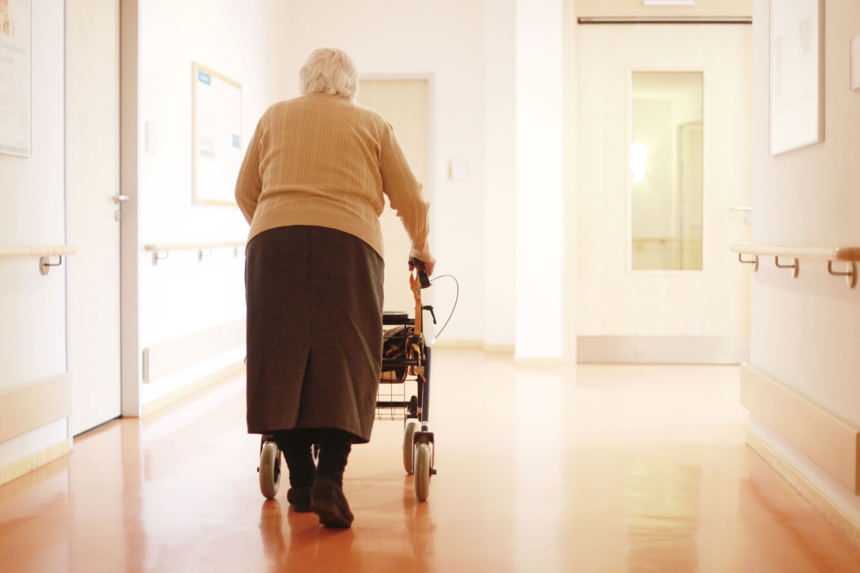 Ein alter Mensch geht mit einem Rollator einen Flur entlang.