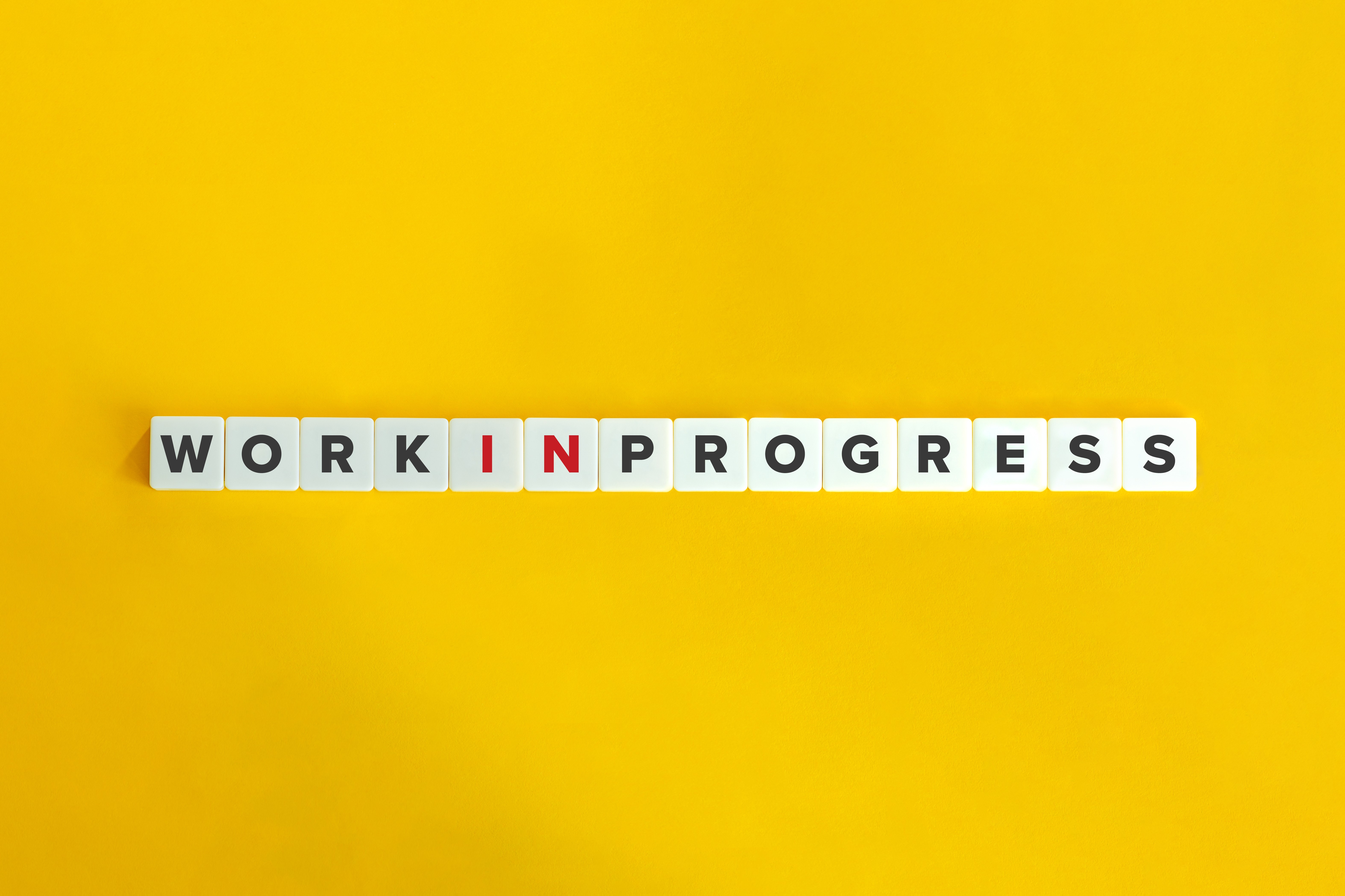 Work in Progress Scrabble-Steine liegen auf einem gelben Untergrund. Sie bilden den Satz: Work in Progress