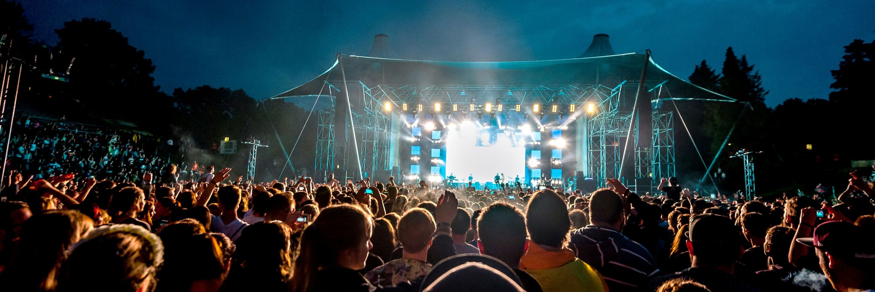 Hell erleuchtete Bühne eines Open-Air-Konzerts, das Publikum ist von hinten zu sehen