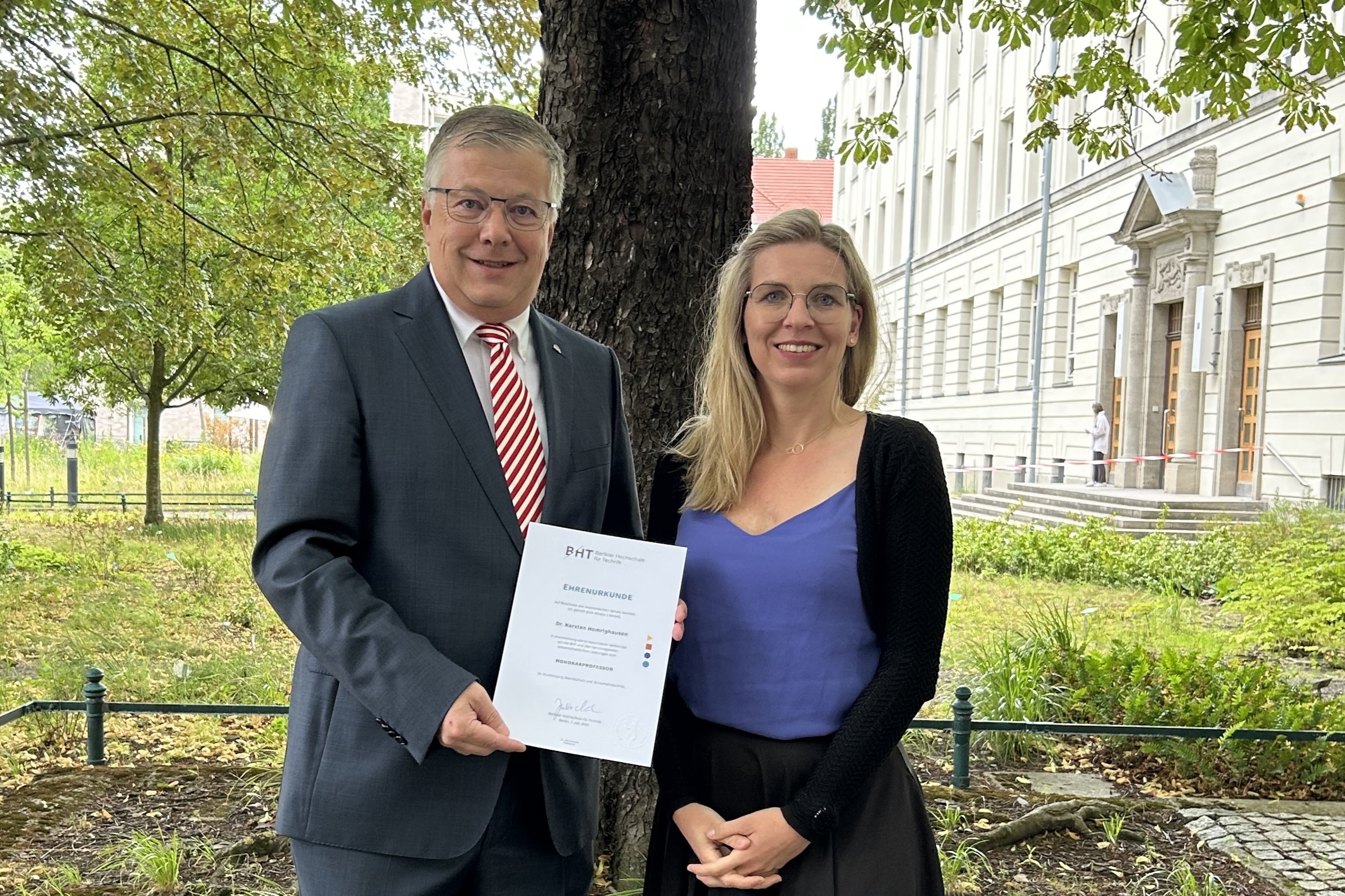 Auf dem BHT-Campus vor dem Haus Beuth und Staudengarten: Karsten Homrighausen hält die Urkunde zur Honorarprofessur, neben ihm steht Julia Neuhaus