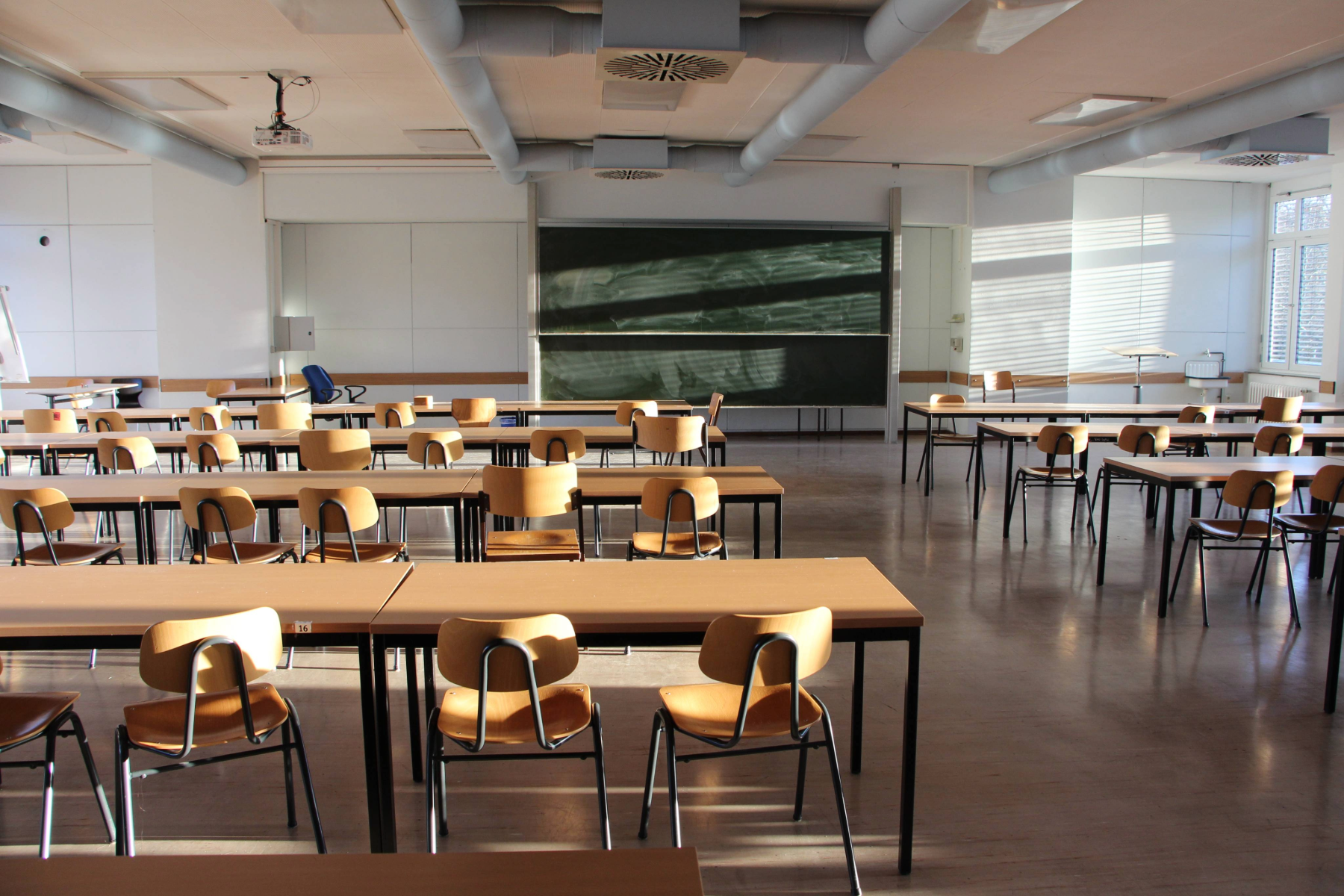 Menschenleerer Raum mit Tischen und Stühlen, die auf eine Tafel ausgerichtet sind