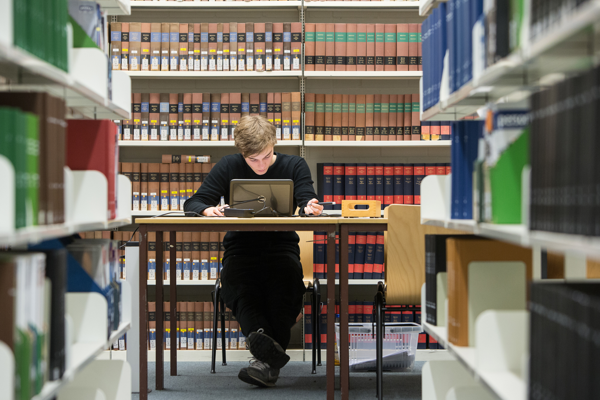 Eine Person sitzt zwischen vielen Bücherregalen an einem Tisch. 