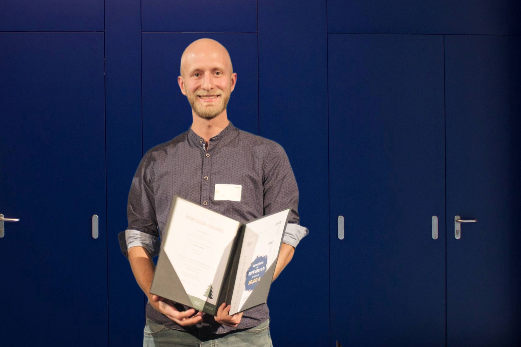 Mann hält eine aufgeklappte Urkundenmappe vor sich und steht vor einer großen blauen Tür