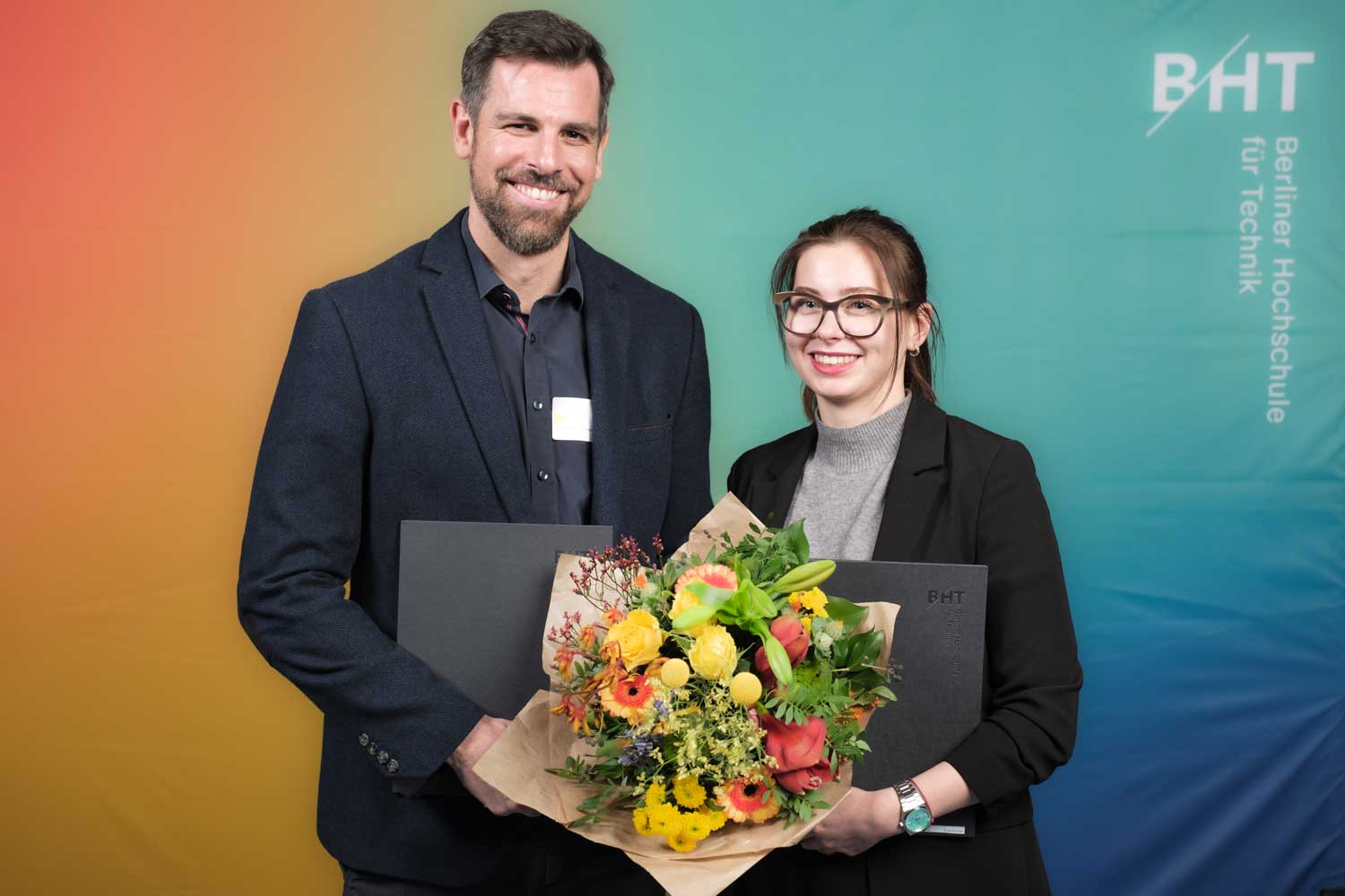 Mann im Anzug und Frau in Blazer stehen nebeneinander und halten gemeinsam einen Blumenstrauß