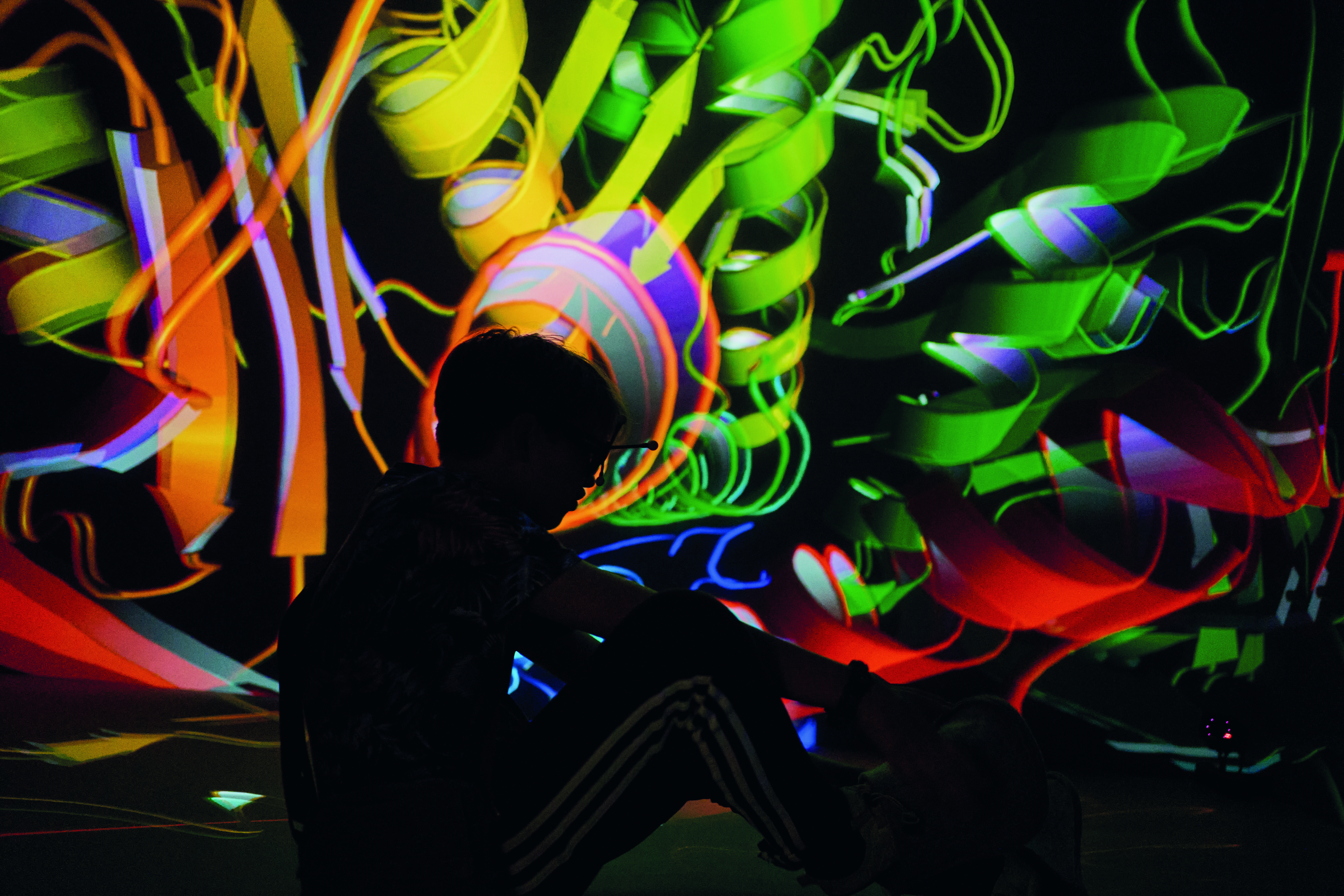 Schatten eines sitzenden Menschen mit VR-Brille vor bunter abstrakter Projektion, Text: Lange Nacht der Wissenschaften, 28. Juni 2025, 17-24 Uhr 
