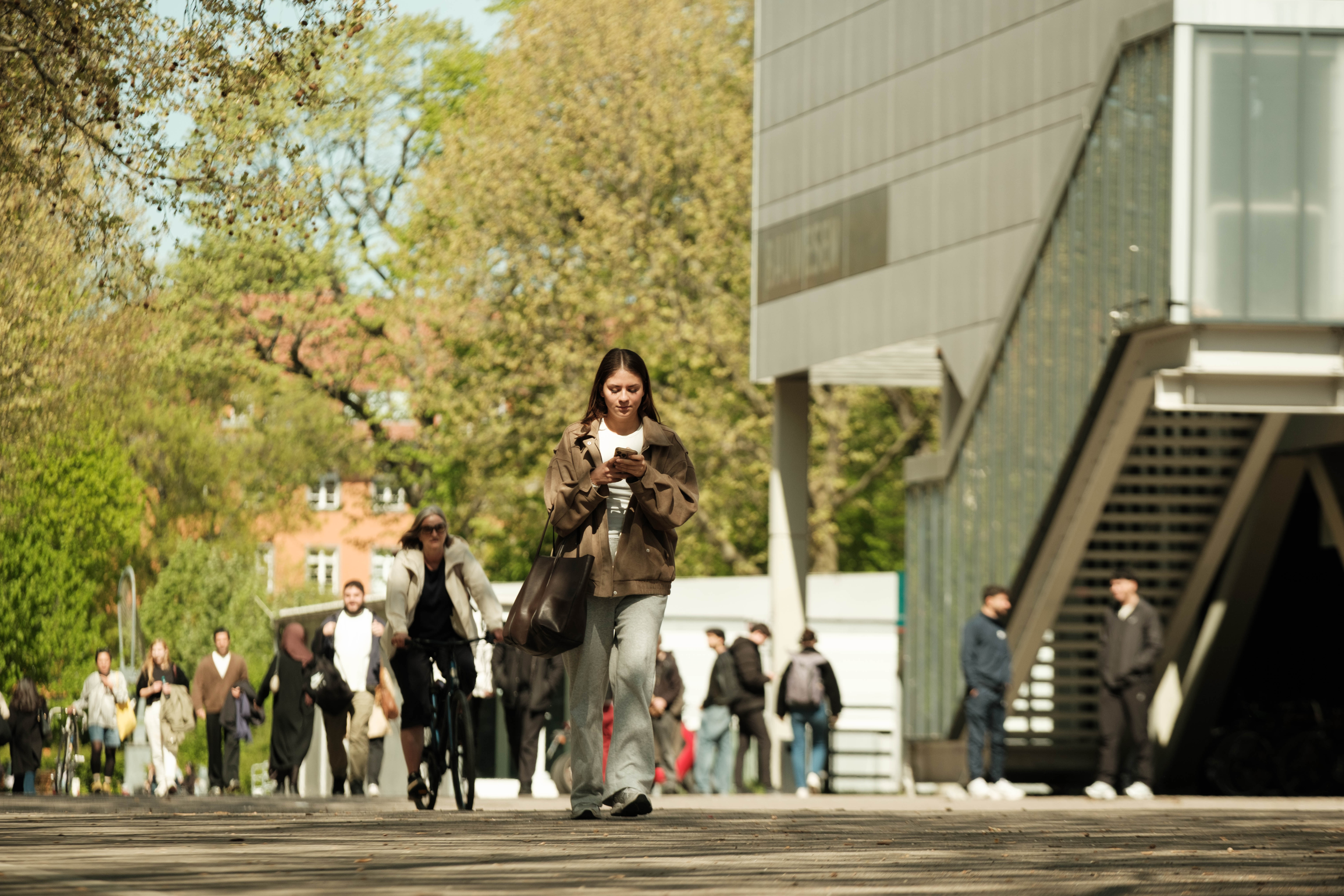 Eine Frau läuft über den belebten Campus der BHT, während sie auf ihr Handy schaut