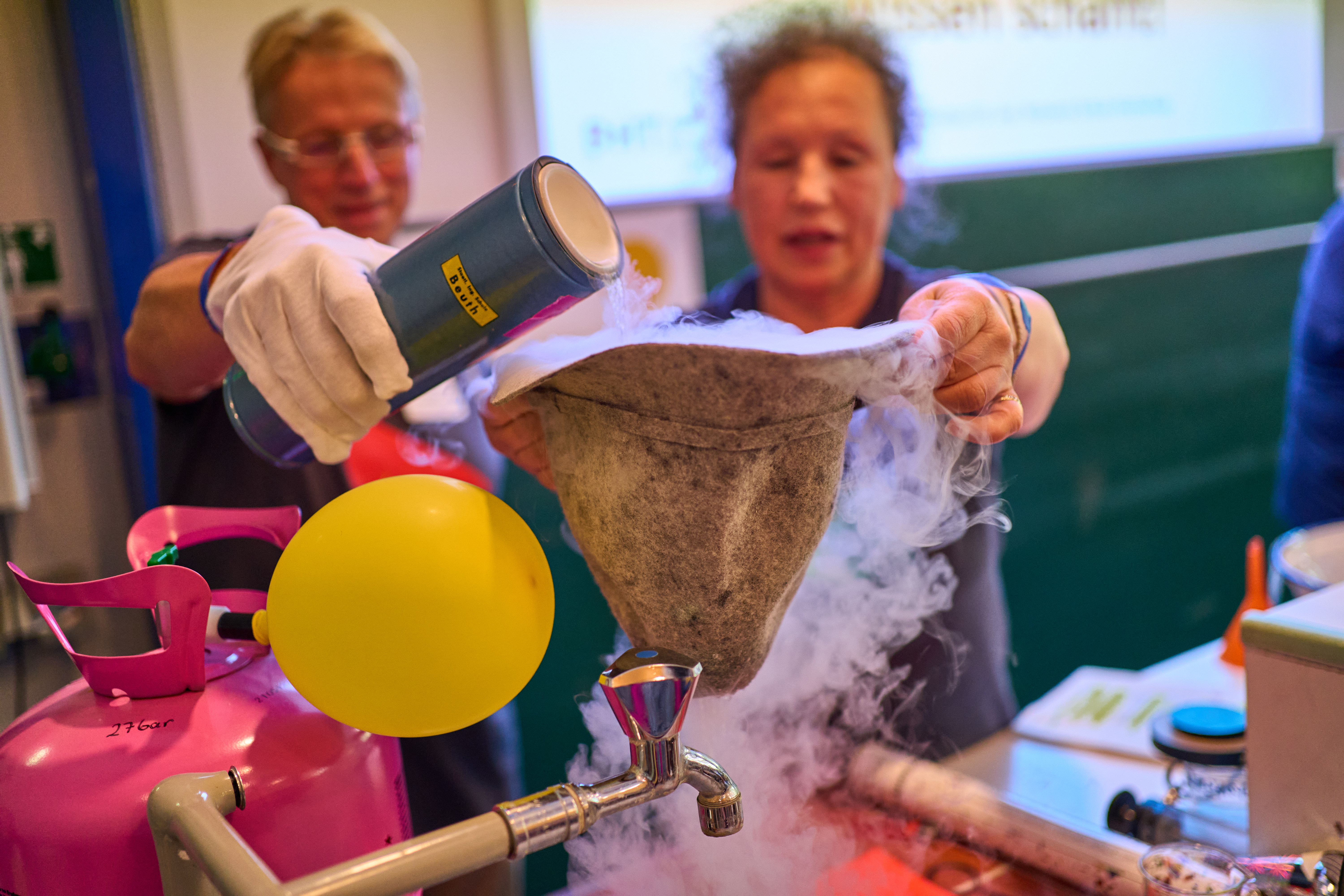 Zwei Personen kippen eine dampfende Flüssigkeit in ein Gefäß