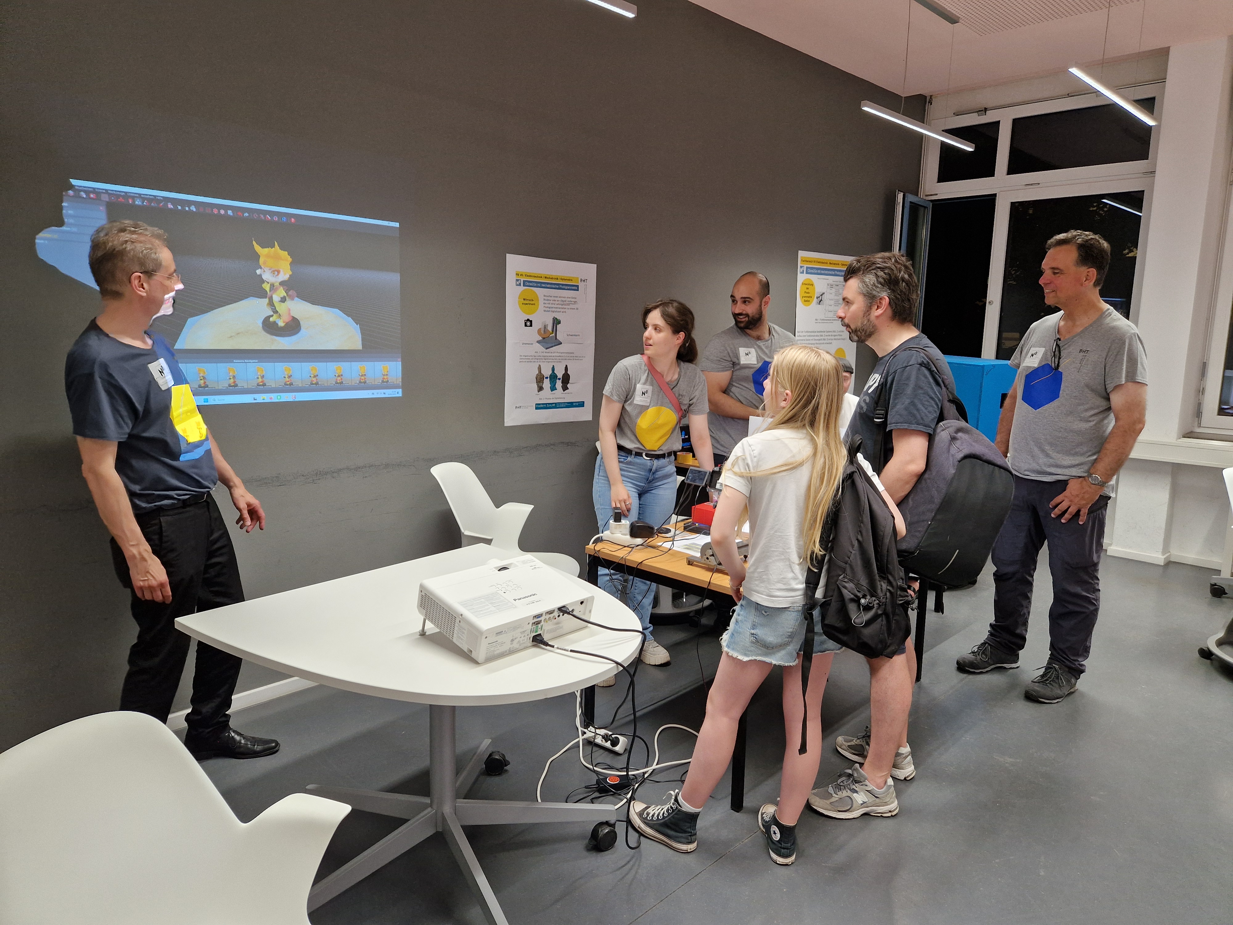 Ein Mann erklärt Besucherinnen eine Projektion an der Wand