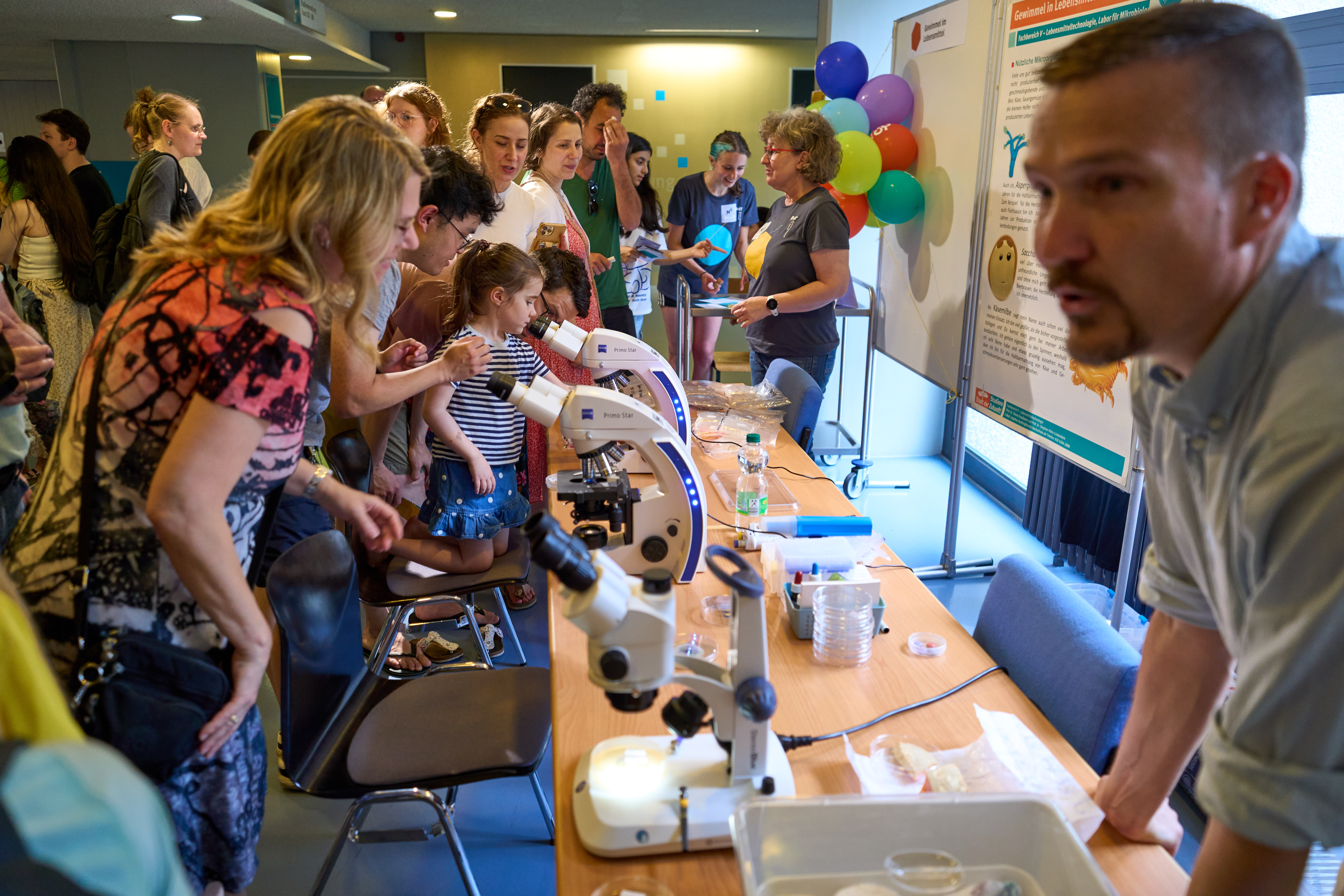 Viele Menschen betrachten einen Stand mit Mikroskopen.