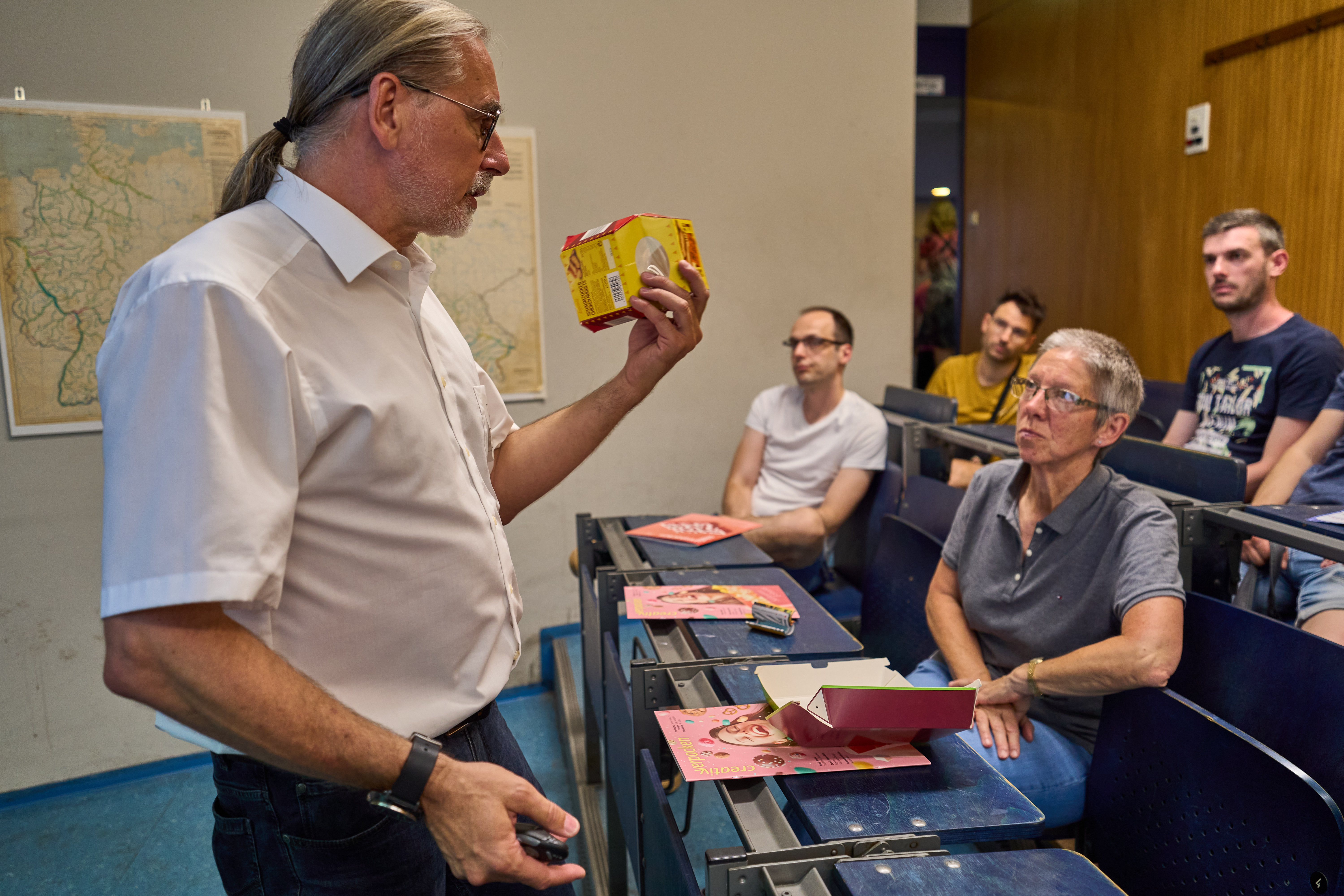 Mann spricht in kleinem Vorlesungssaal und hält eine Verpackung.