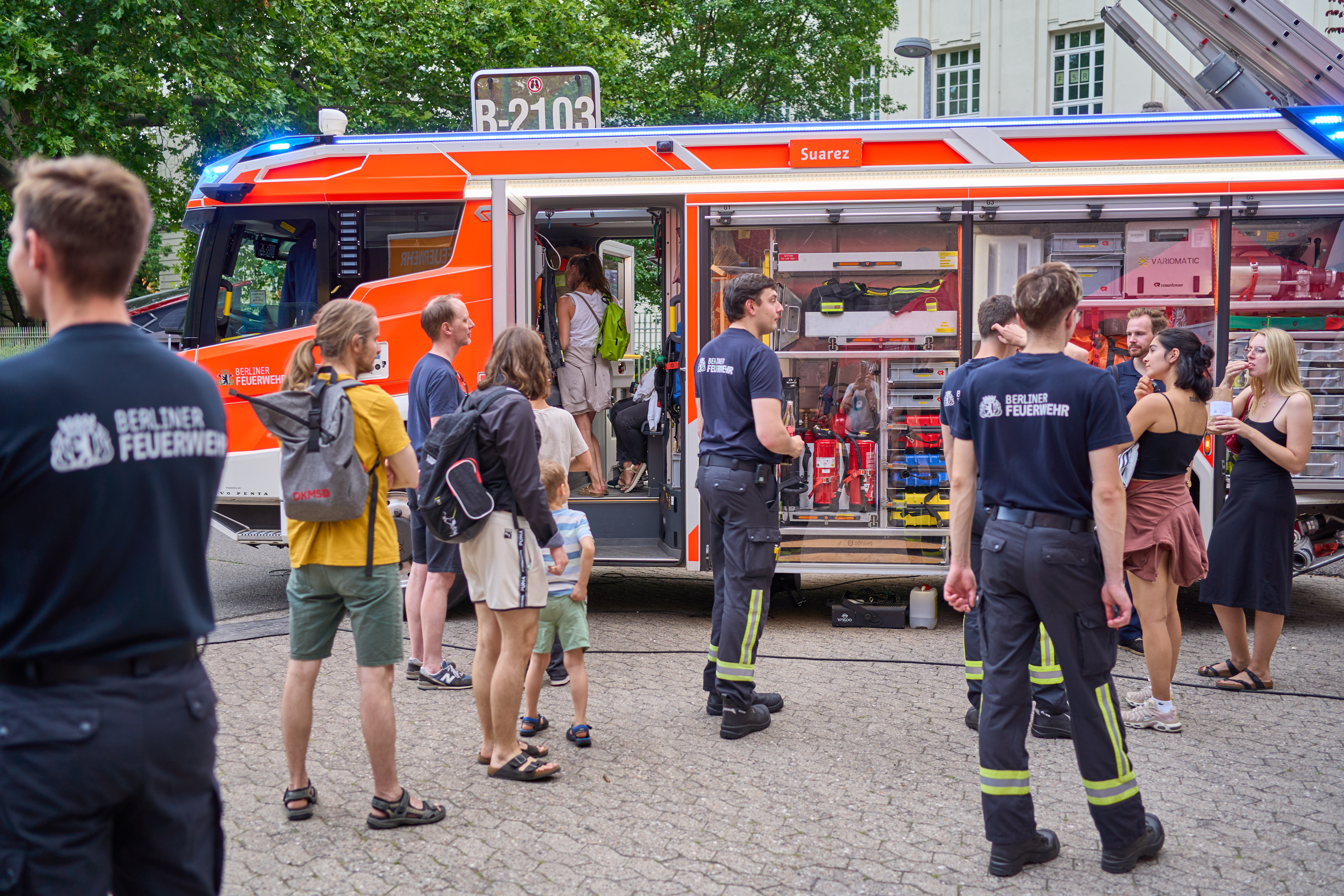 Menschen stehen vor dem Einsatzfahrzeug der Berliner Feuerwehr.