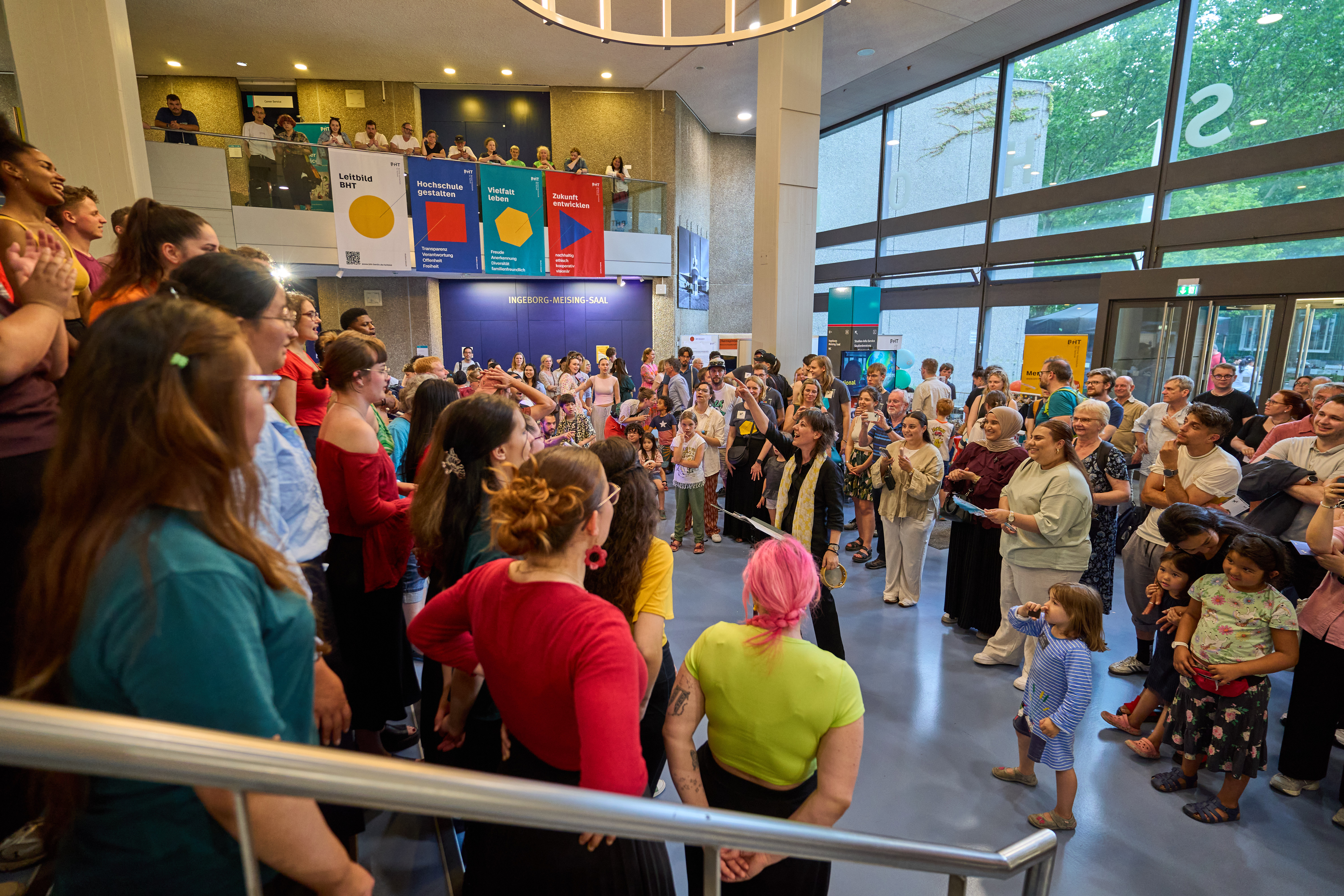 Chor singt auf einer Treppe im Foyer vor Publikum.