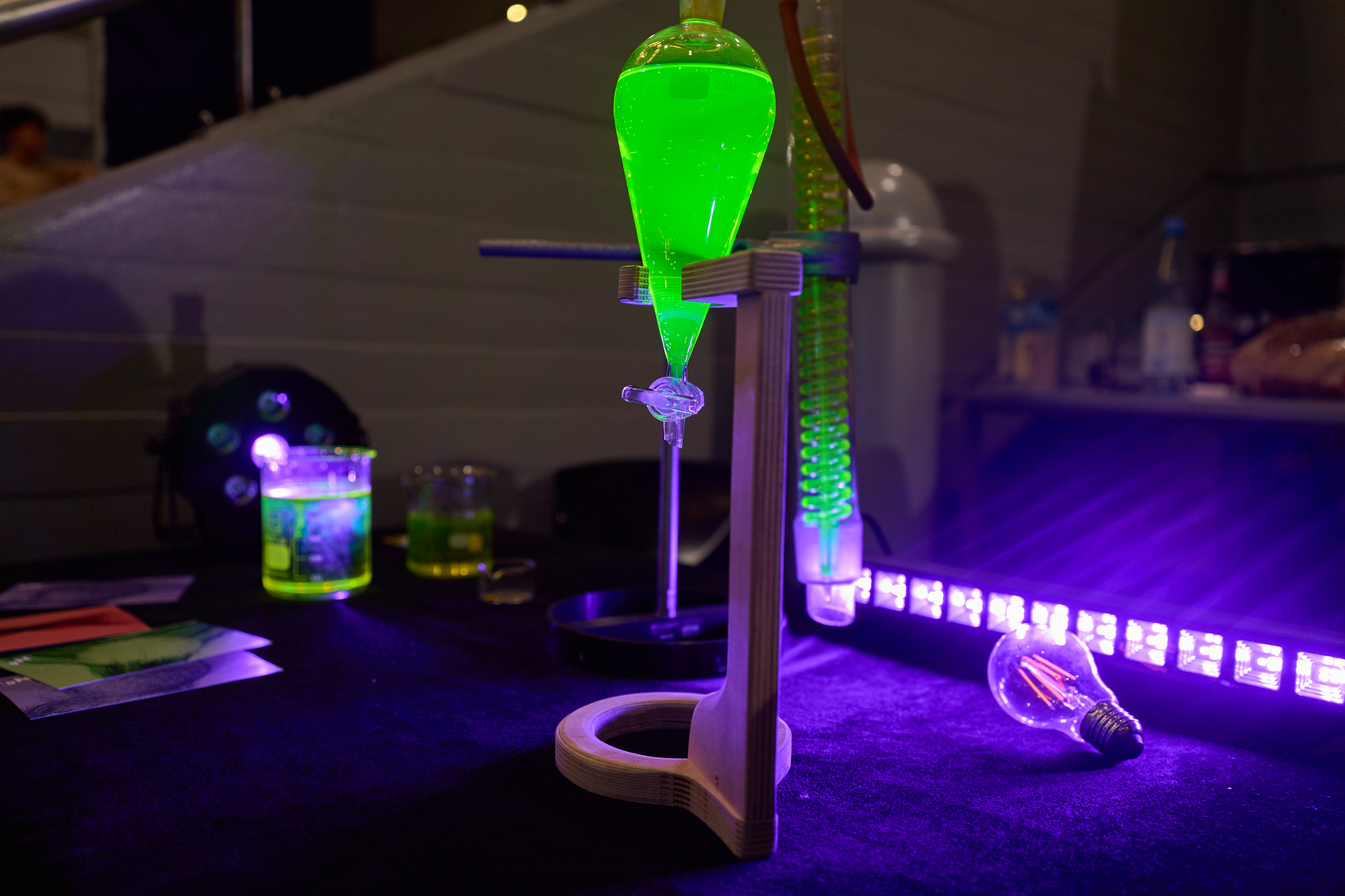 Durchsichtiges Glasgefäß mit leuchtend fluoreszierender Flüssigkeit, die in dunkler Umgebung strahlt.