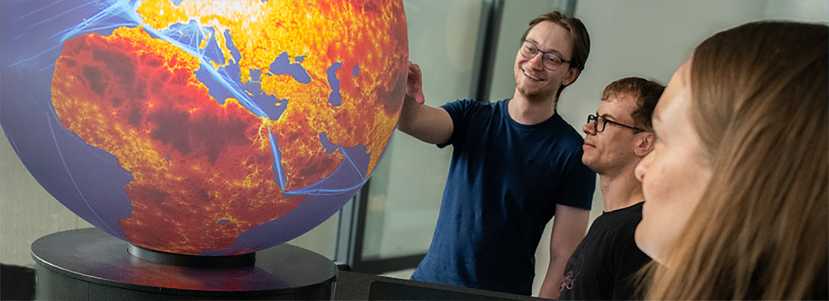 Drei Studierende blicken auf einen erleuchteten Globus