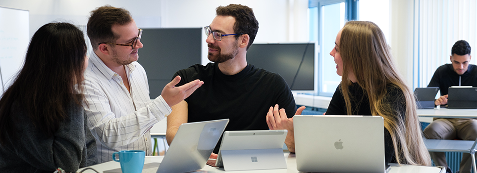 vier Studierende sitzen an einem Tisch und diskutieren